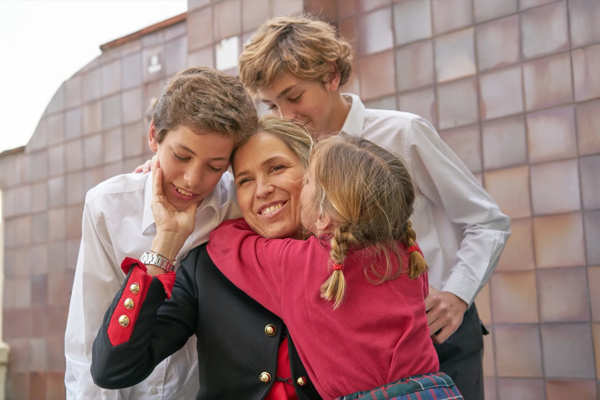 A mother hugging her three children in school uniform