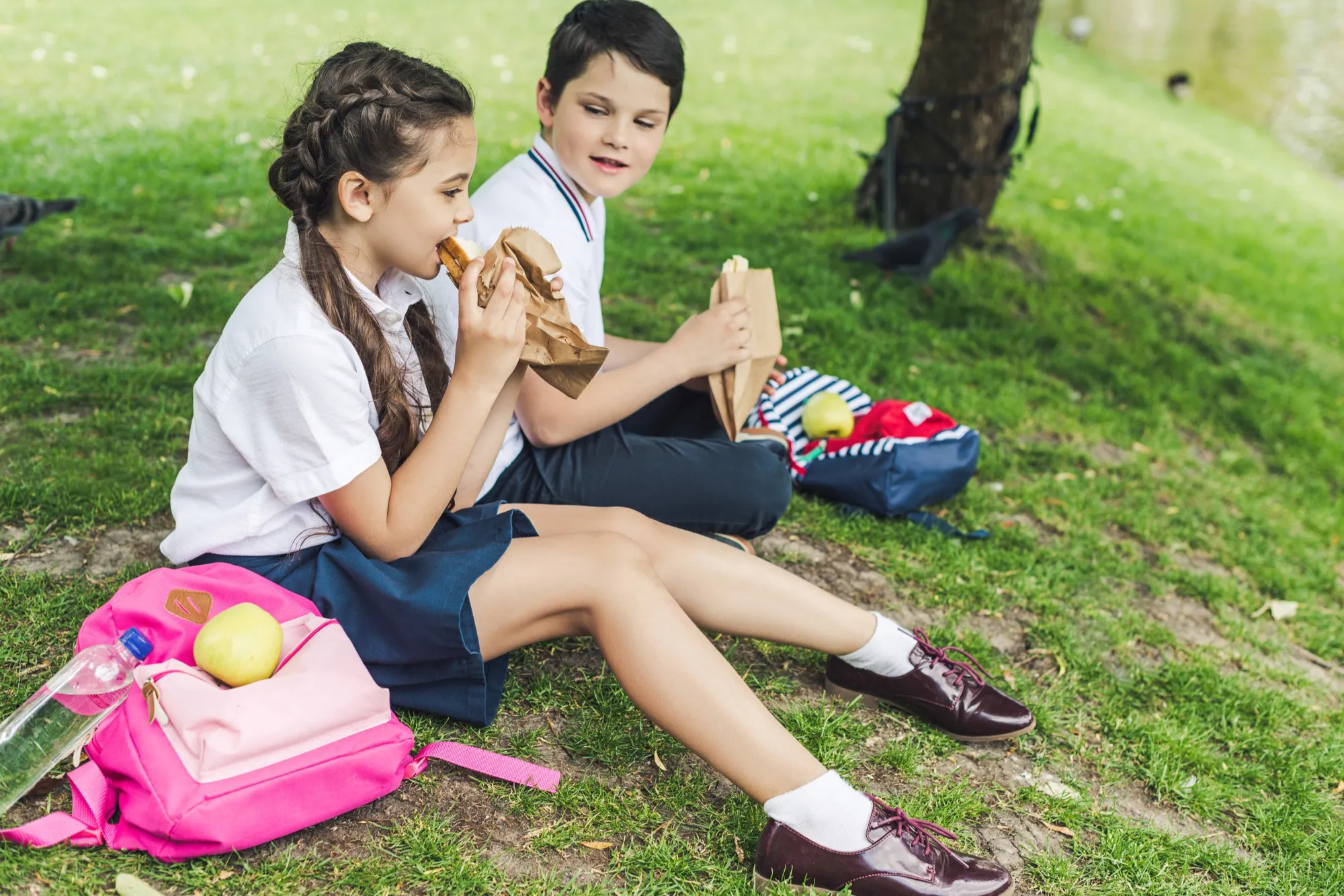Two students in school uniform eating lunch on the grass